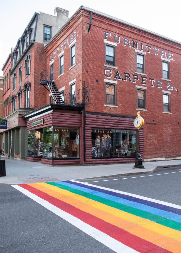 A city street with red brick buildings and a crosswalk painted like a rainbow.