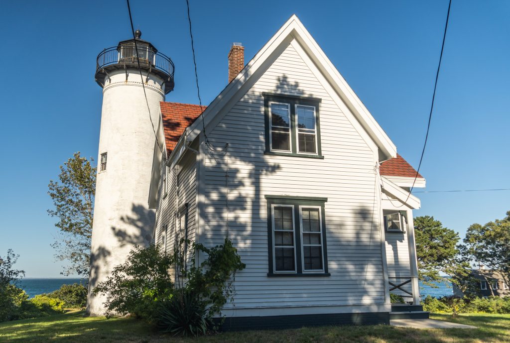 A small White House attached to a tall white lighthouse on a sunny day.