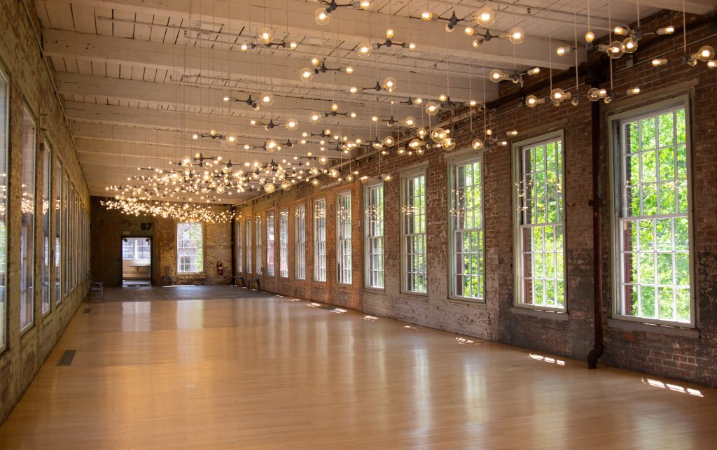 A long hallway in a window-filled mill with black and white lights hanging from the ceiling.