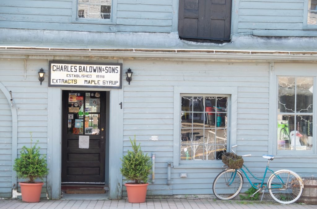 An old fashioned blue-gray building with a sign advertising maple syrup and a bike parked in front.