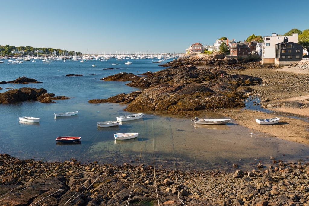 A rocky section of the beach in Marblehead MA with some small boats close to shore